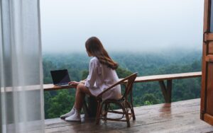 A woman using and working on laptop computer while sitting on balcony with a beautiful nature view